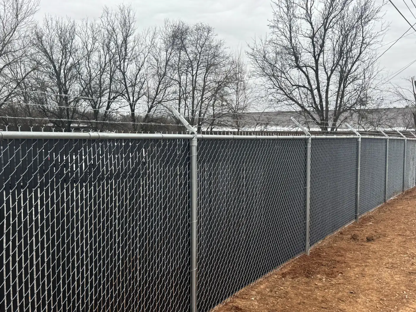 Commercial chain-link fence with black privacy slats and razor wire — S&S Fencing