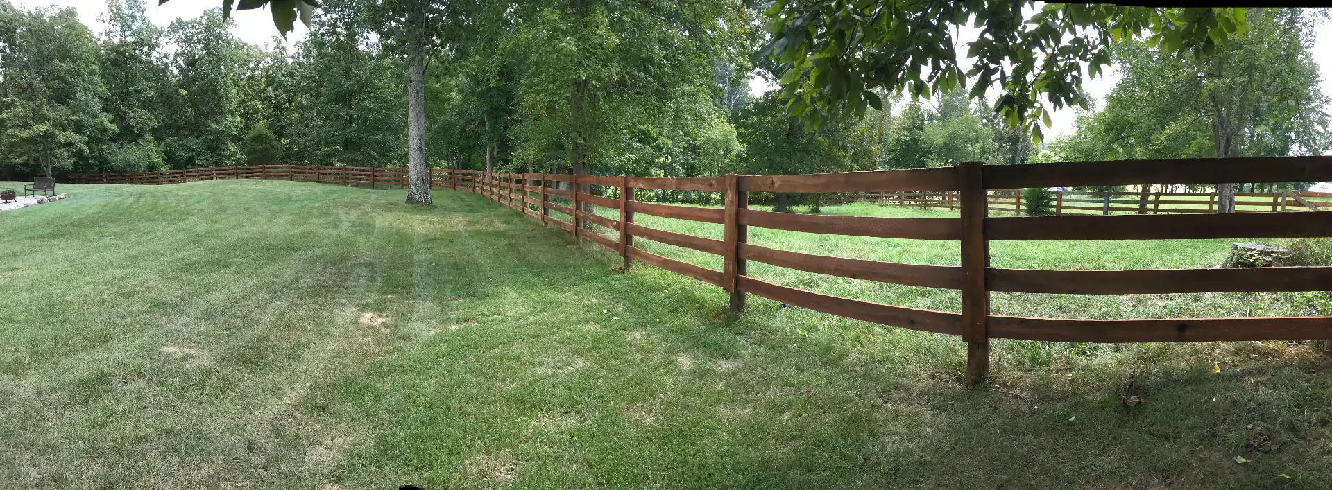 Stained wood board paddock fence through a Kentucky tree line — S&S Fencing
